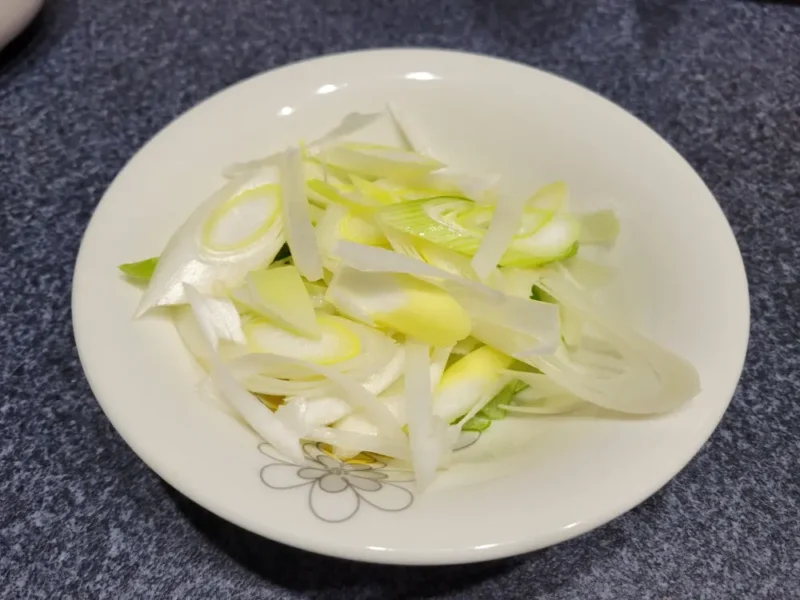 斜め薄切りにした長ねぎをまな板の上に並べた様子