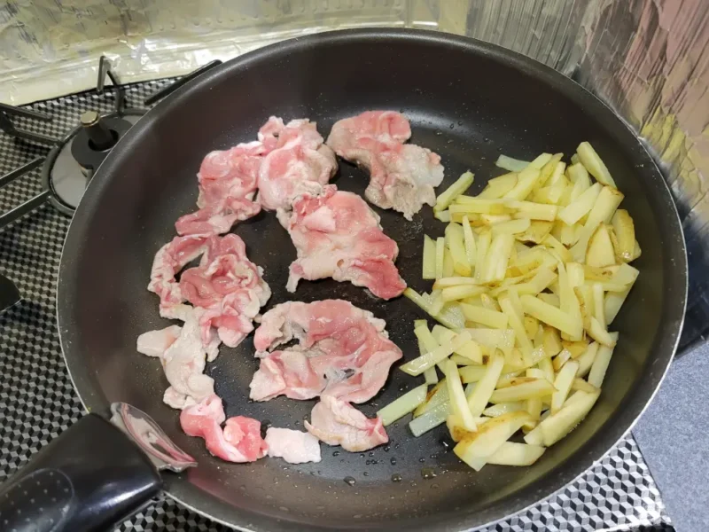 じゃがいもを炒めたフライパンに豚切り落としを加えている様子