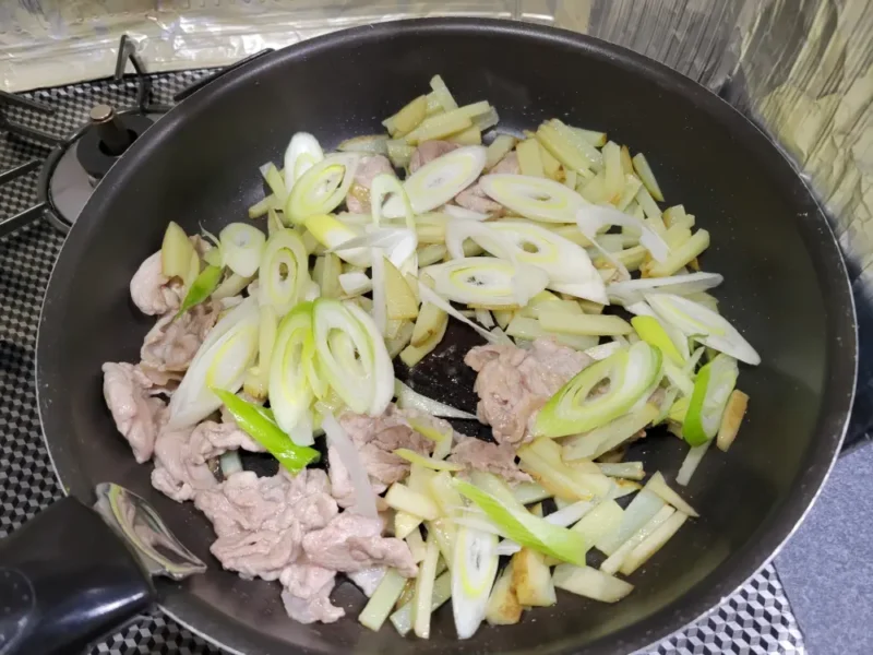 豚肉とじゃがいもを炒めたフライパンに長ねぎを加えた様子