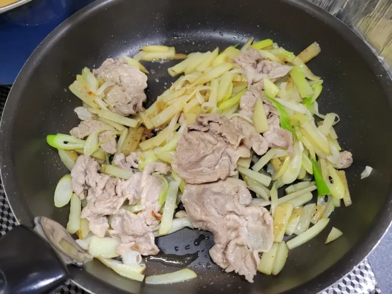 豚肉と新じゃがと長ねぎの炒め物に塩だれを加えて仕上げている様子