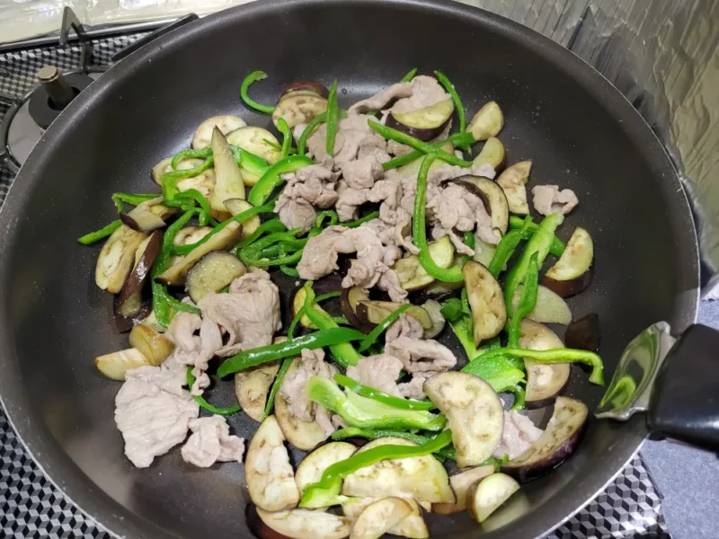 豚肉となすを炒めたフライパンにピーマンを加えた様子