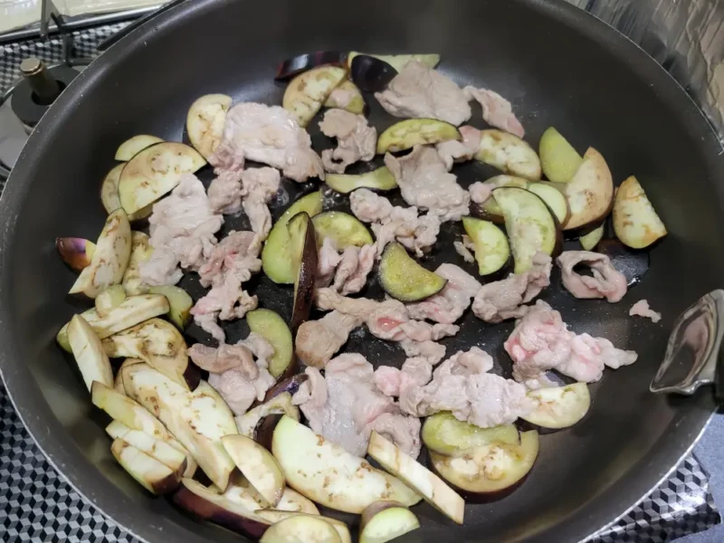 炒めたなすのフライパンに豚切り落としを加えている様子