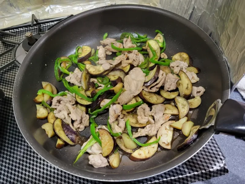 豚肉となすとピーマンの炒め物に甘辛しょうゆだれを加えて仕上げている様子
