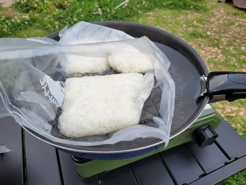 キャンプ場でコンパクトグリルのフライパンにジップロックのご飯を入れて温めている様子